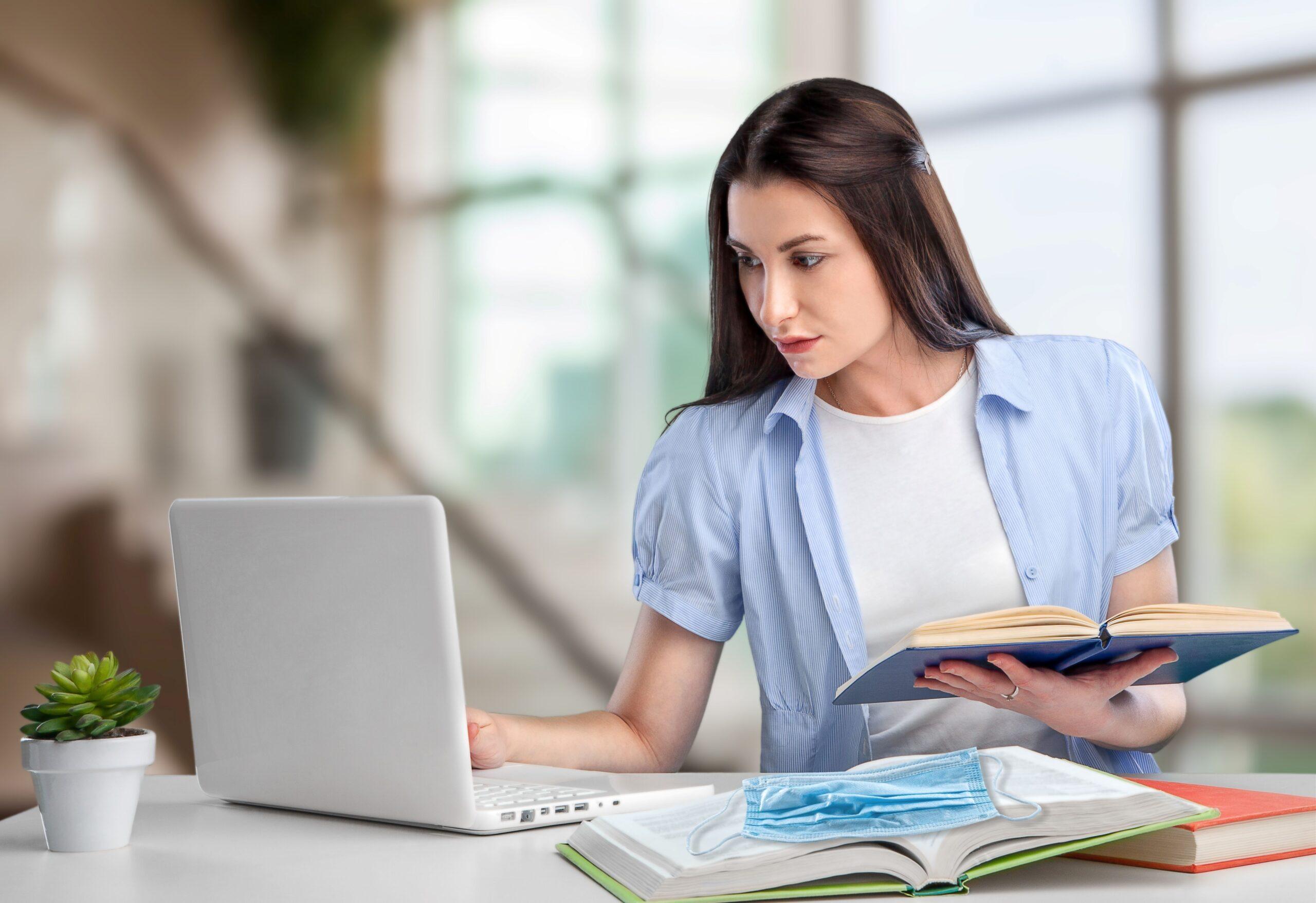 Frau lernt am Laptop mit Buch und Maske auf dem Tisch – digitales Lernen und Hygienebewusstsein in der Weiterbildung